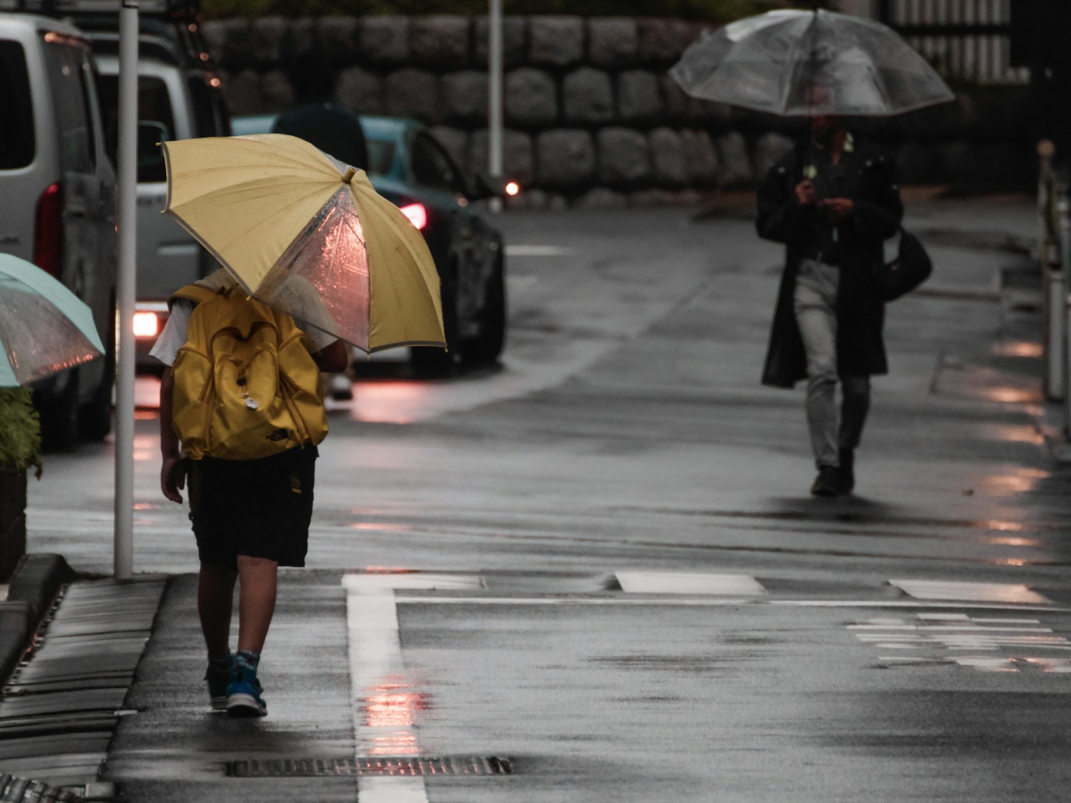 Enfant avec un parapluie jaune marchant sous la pluie aux côtés d'autres personnes avec des parapluies