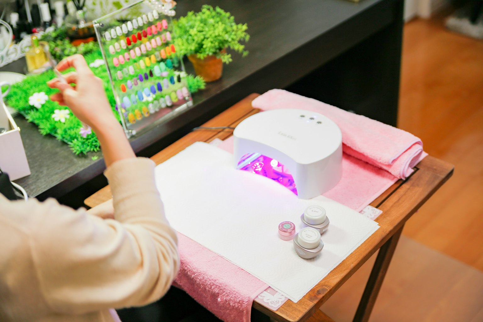 Escena de salón de uñas con una mano aplicando esmalte bajo una lámpara UV y esmaltes coloridos