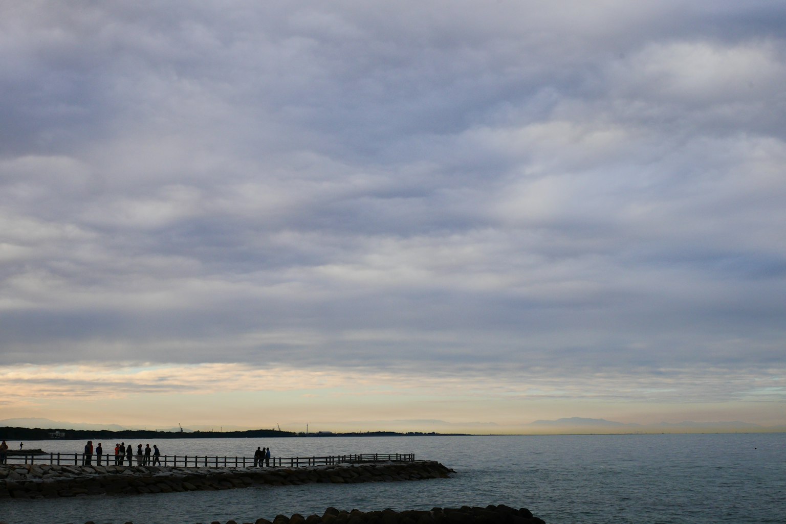 Menschen stehen am Ufer mit blauem Meer und bewölktem Himmel