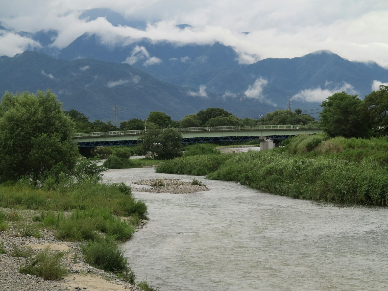 Pemandangan dengan sungai dan jembatan dengan pegunungan dan awan yang indah di latar belakang