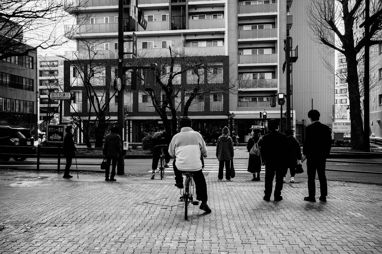 Escena urbana en blanco y negro con personas reunidas una persona en bicicleta y edificios visibles