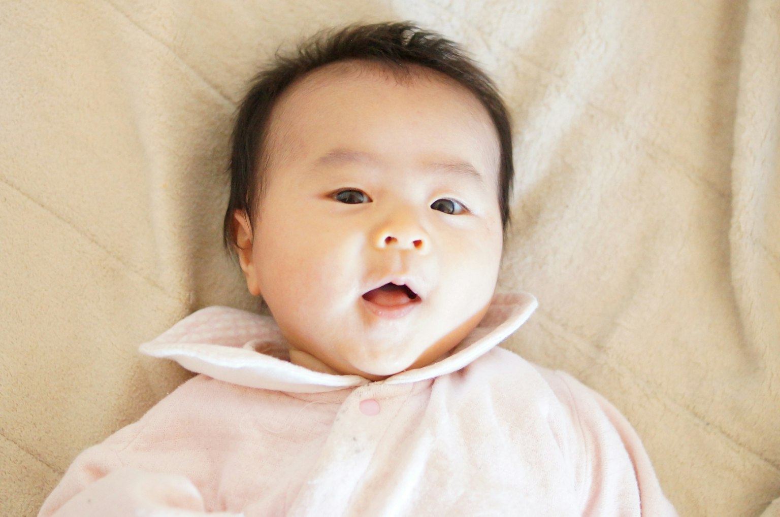베이지색 담요 위에 누워 있는 아기의 행복한 표정
