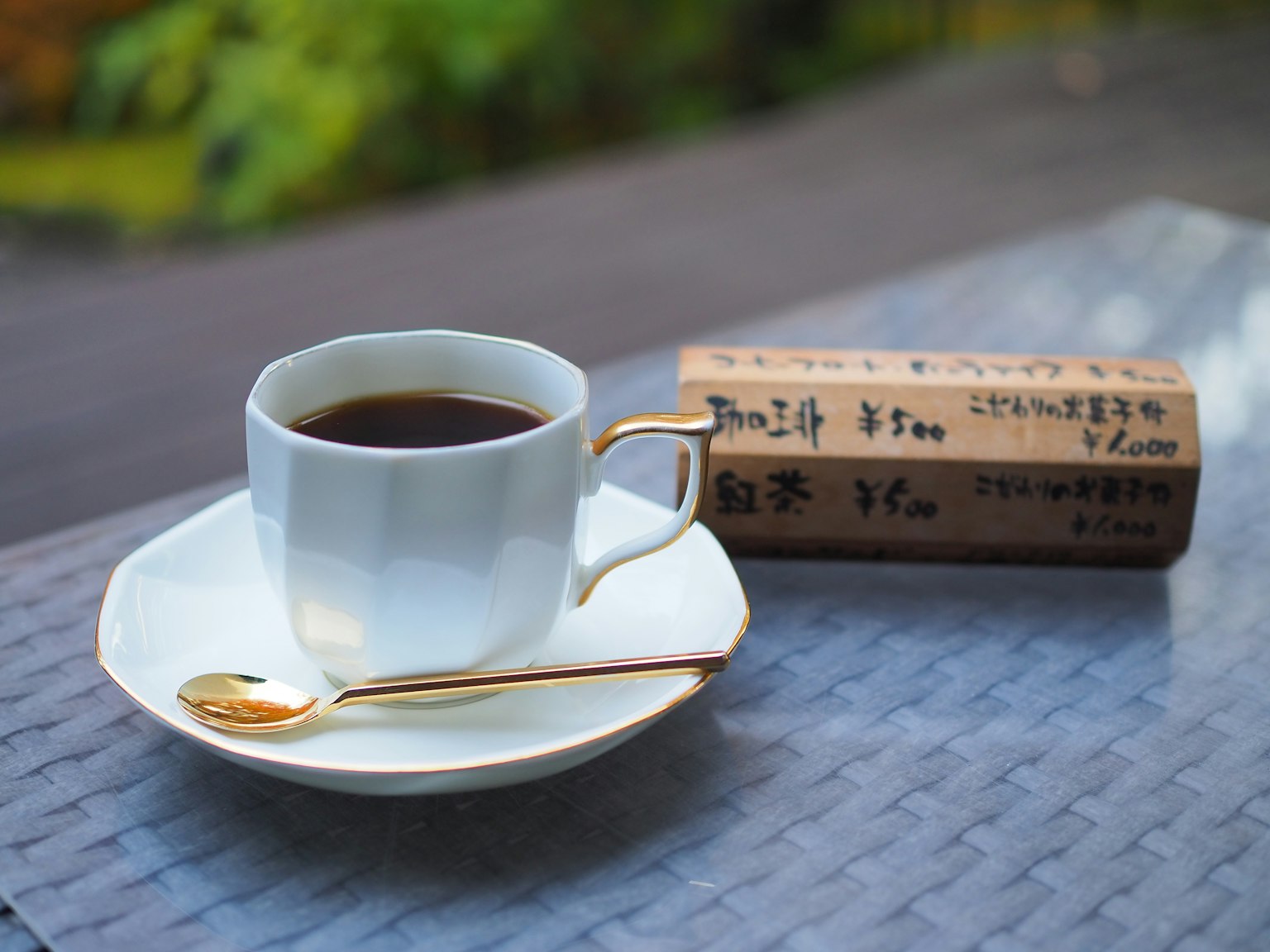 Una tazza di caffè bianca piena di caffè accompagnata da un cucchiaio dorato su un tavolo