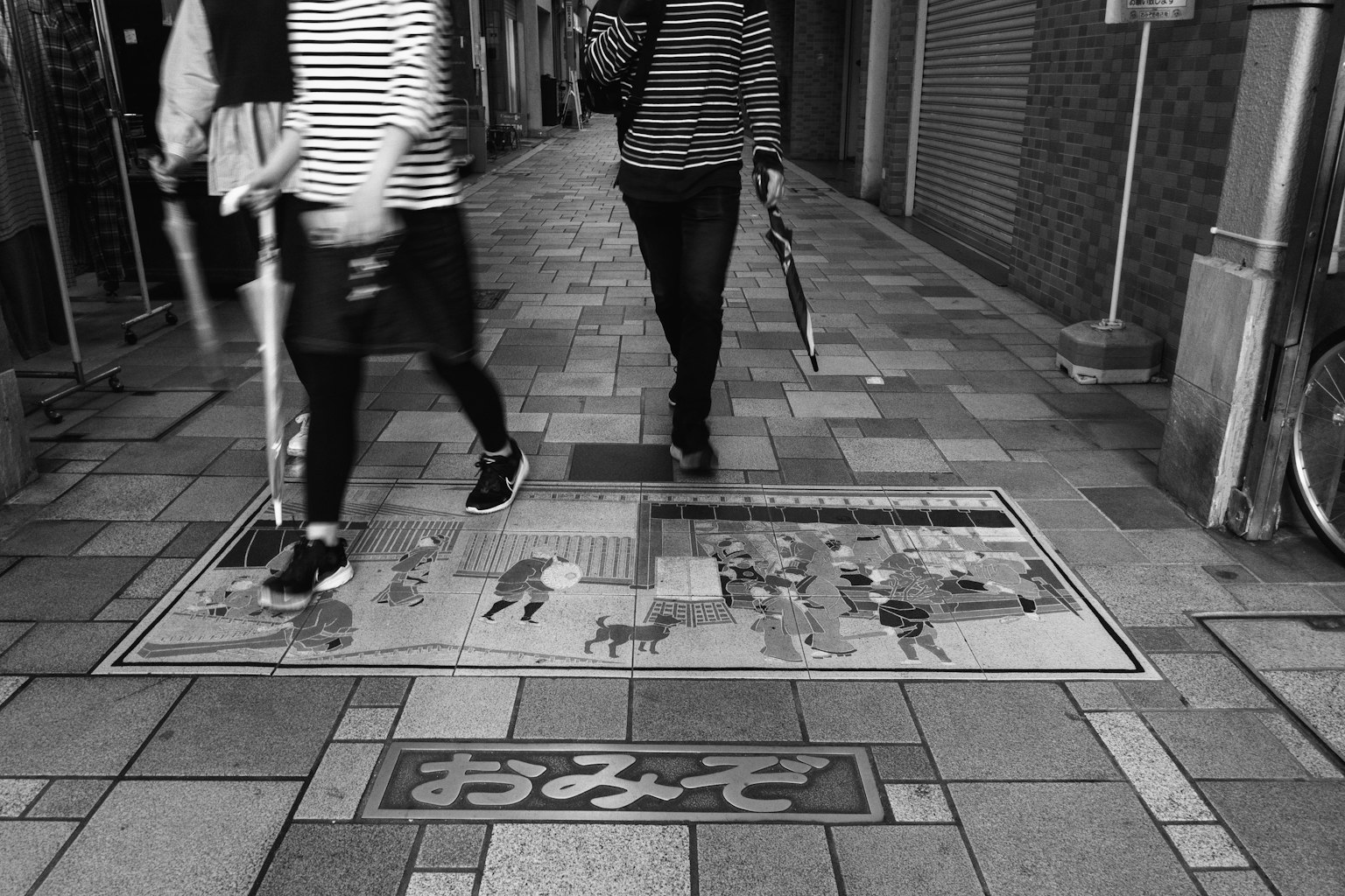 Dos personas con ropa a rayas caminando en una calle en blanco y negro con arte en el suelo colorido