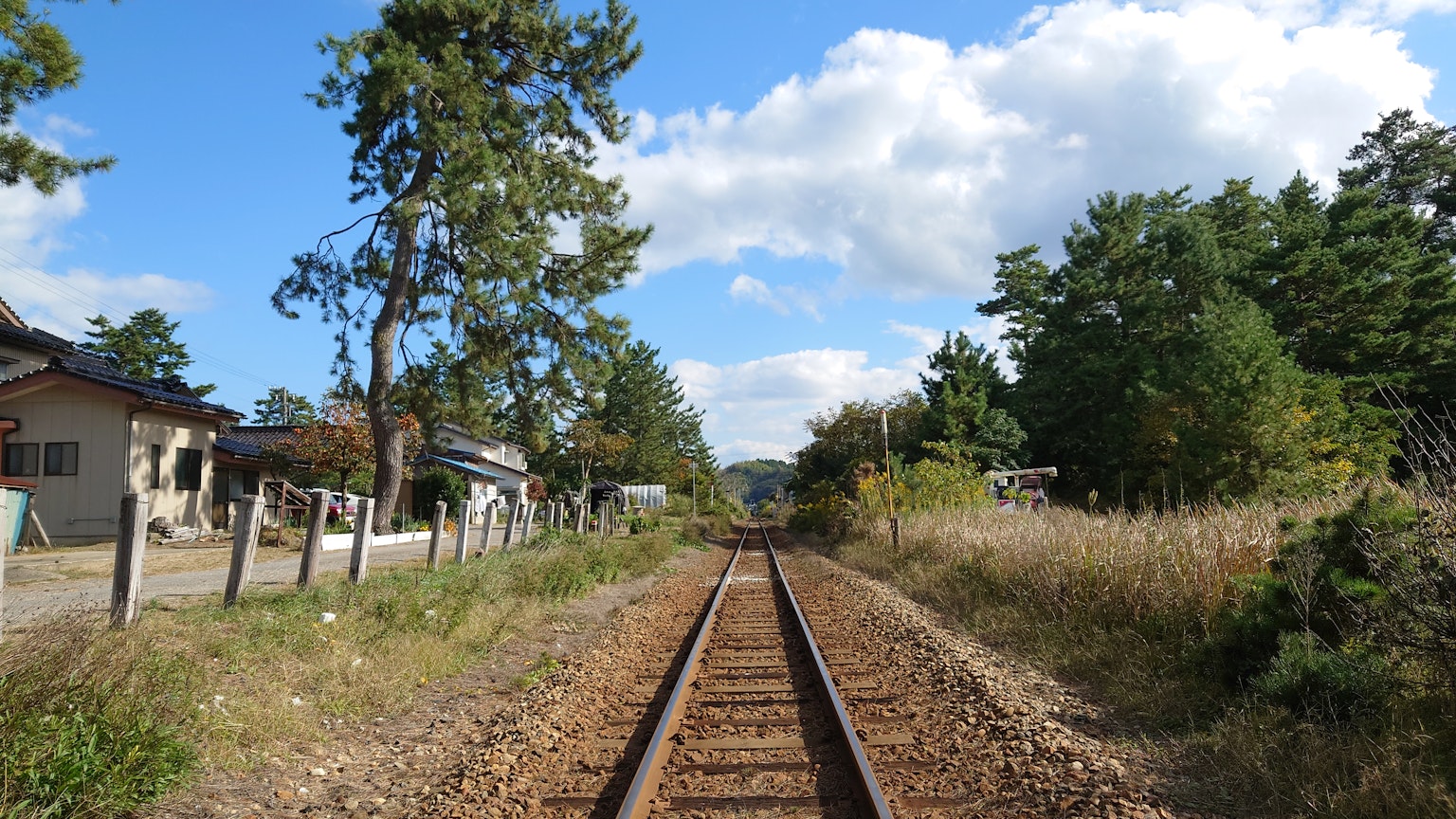 View of railway tracks leading into the distance surrounded by trees and blue sky