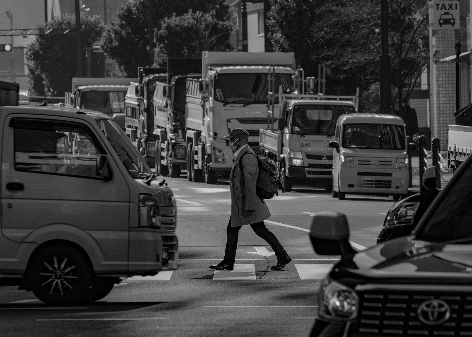 モノクロの街中で、交通が多い交差点を横断する人物