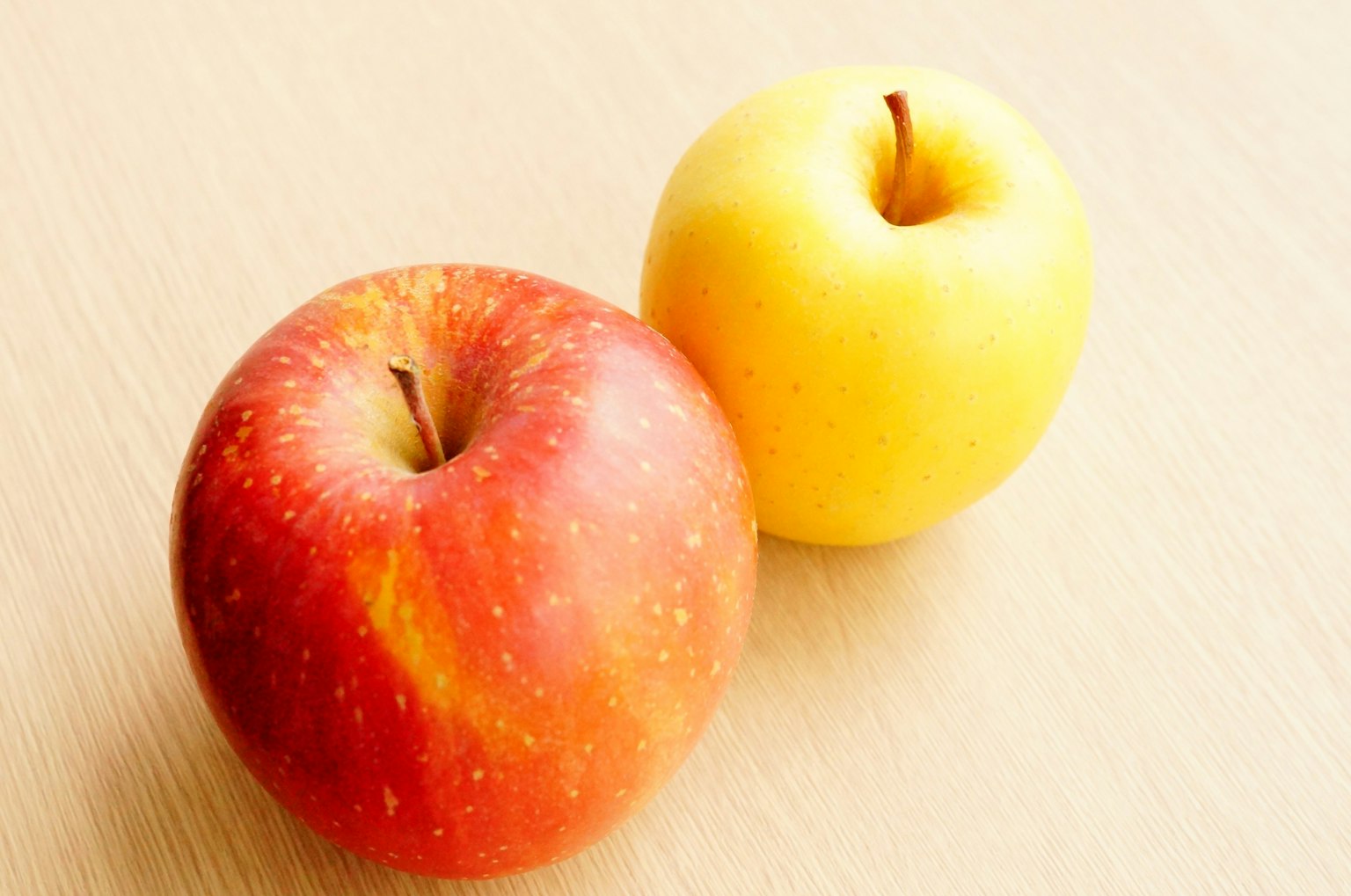 Une pomme rouge et une pomme jaune posées sur une surface claire