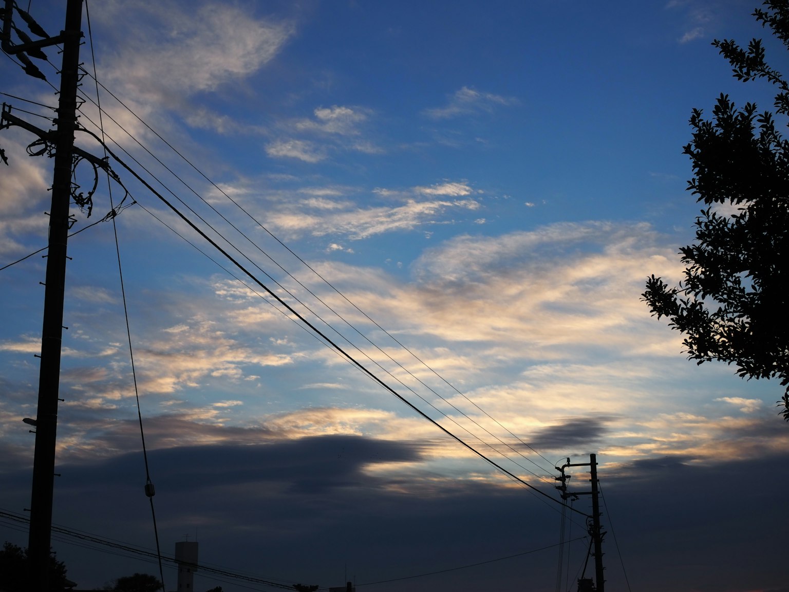 Siluet tiang listrik di latar belakang langit biru dengan awan