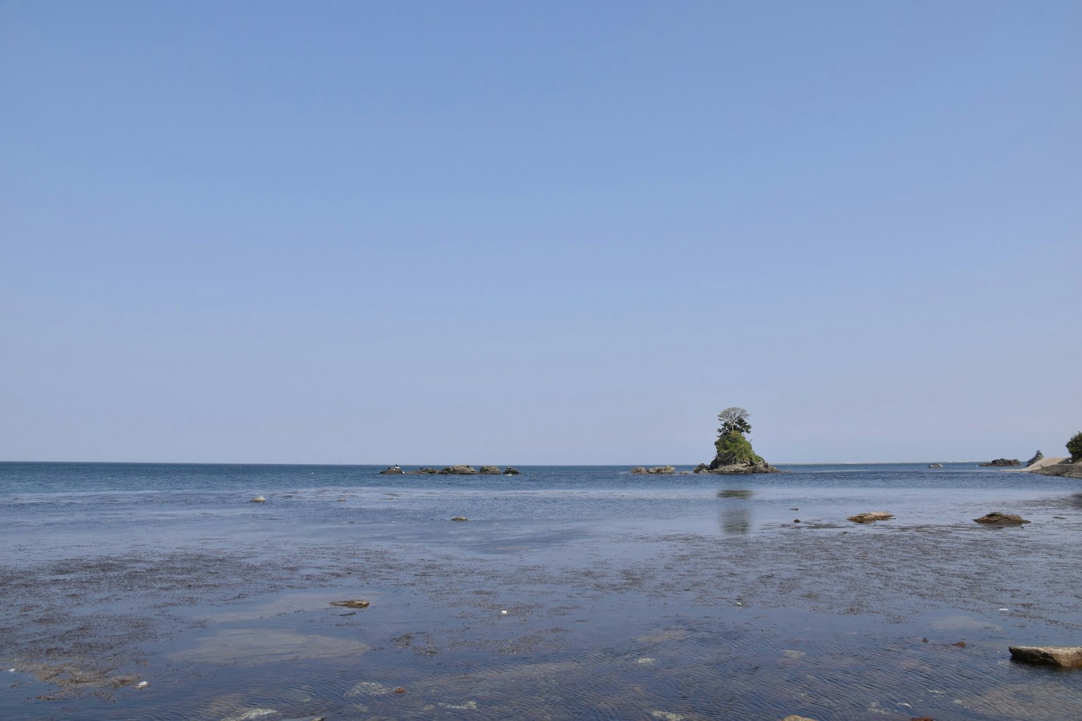 Mare calmo con cielo blu che presenta un'isola piccola e rocce