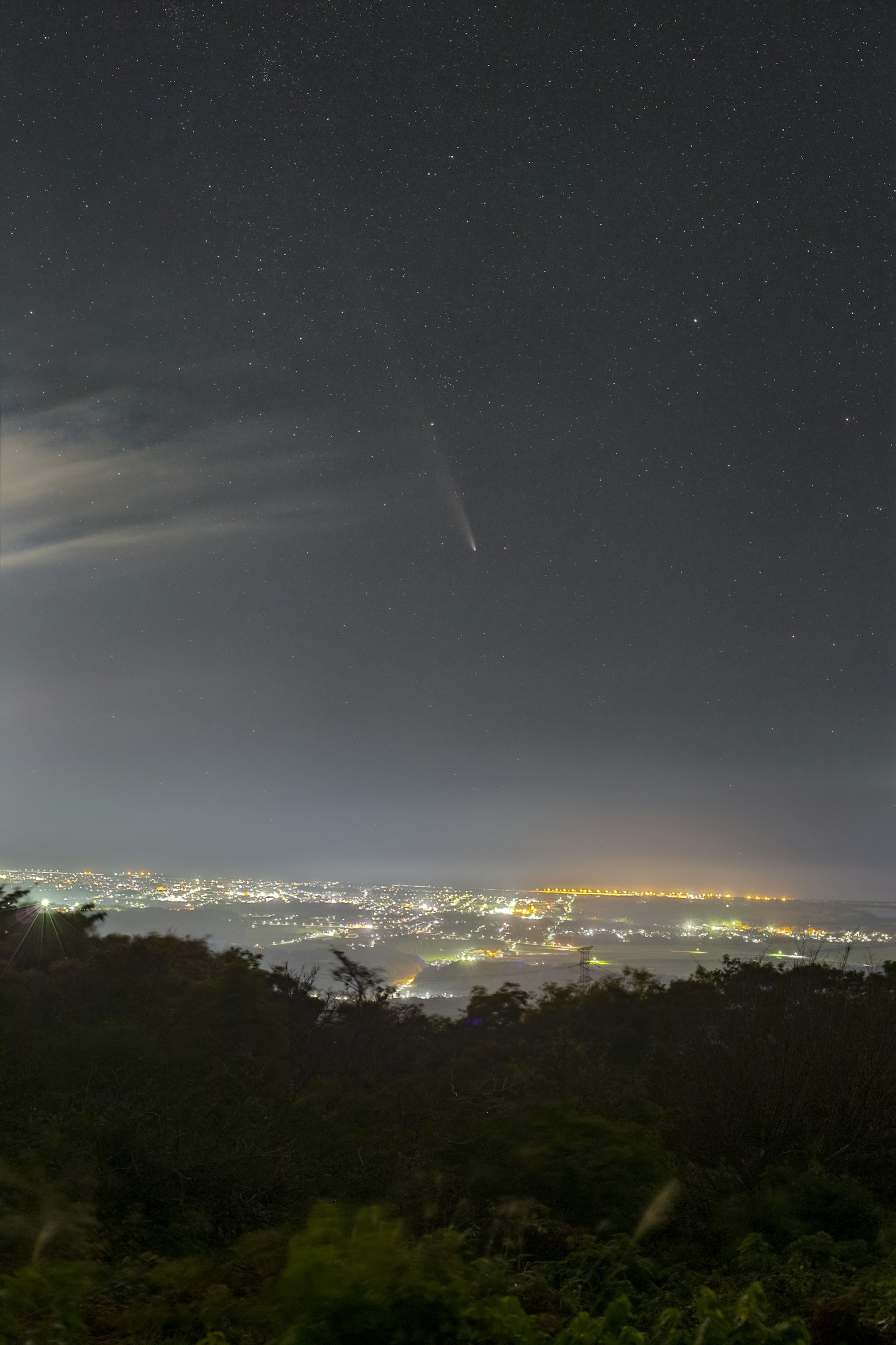 Night sky filled with stars and city lights with a visible comet