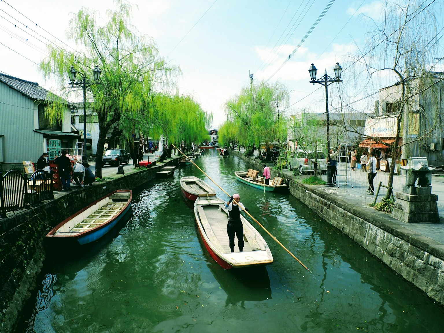 Un pescador remando en un canal tranquilo rodeado de sauces verdes