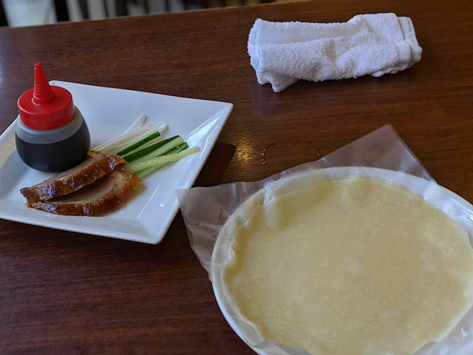 Irisan daging bebek dengan bawang hijau dan botol saus di piring dengan adonan tipis
