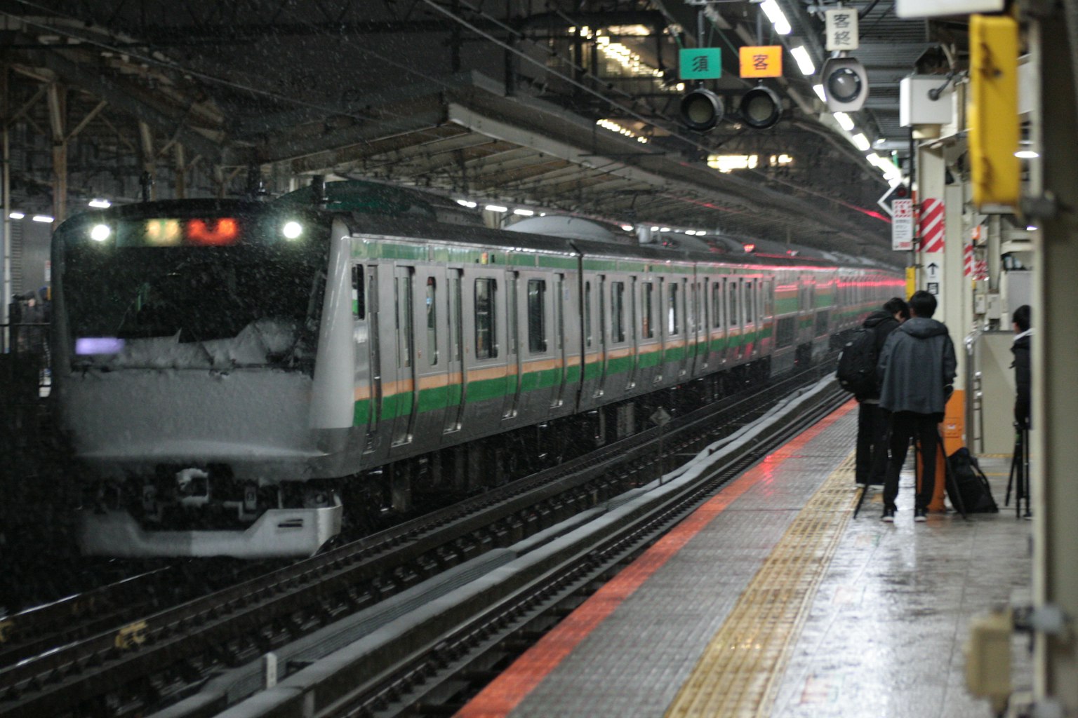 Scena di un treno in arrivo alla stazione con un treno a strisce verdi e persone in attesa