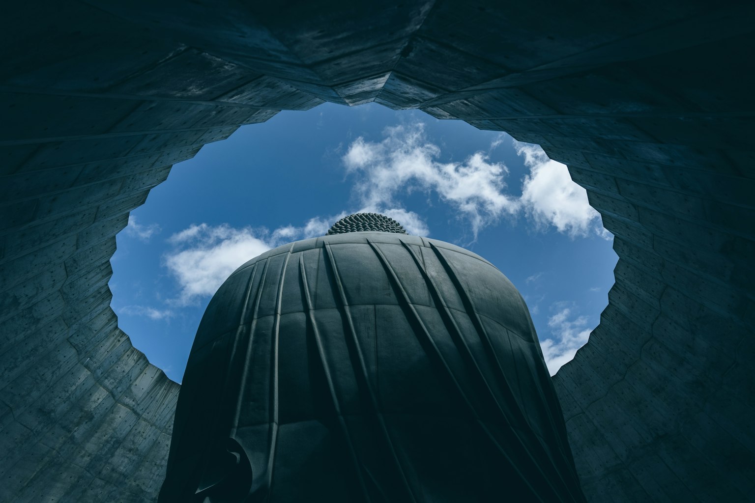 View of a large Buddha statue from below with blue sky and clouds
