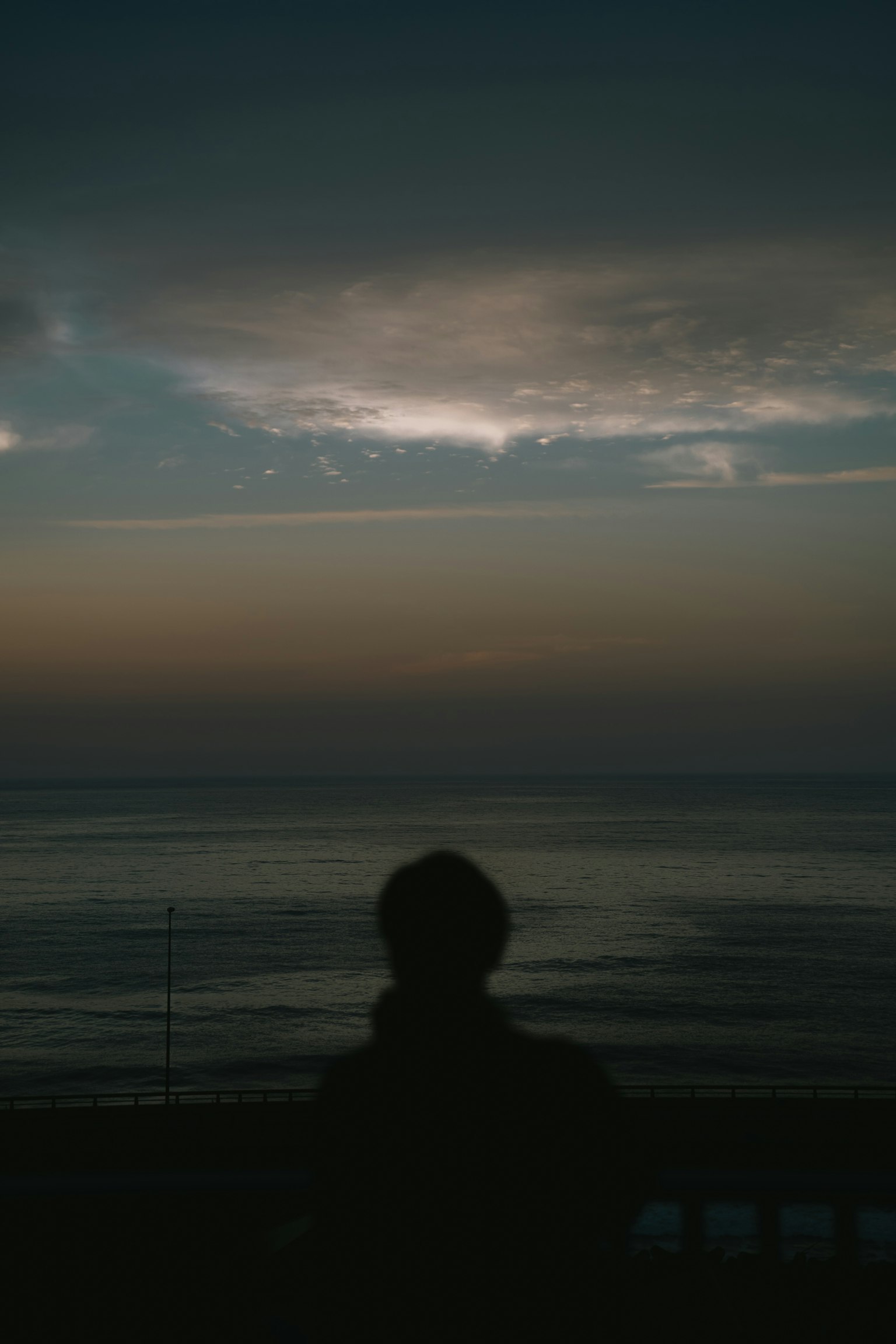 Silhouette d'une personne regardant la mer sous un ciel sombre