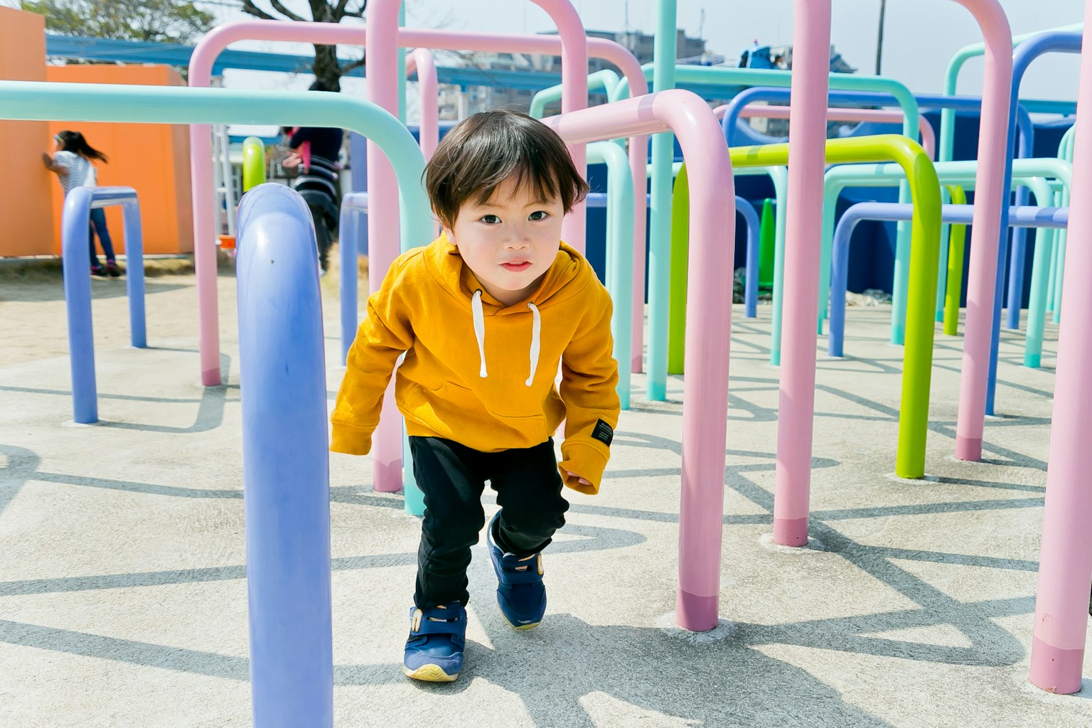 Seorang anak mengenakan hoodie kuning bermain di struktur taman bermain berwarna-warni