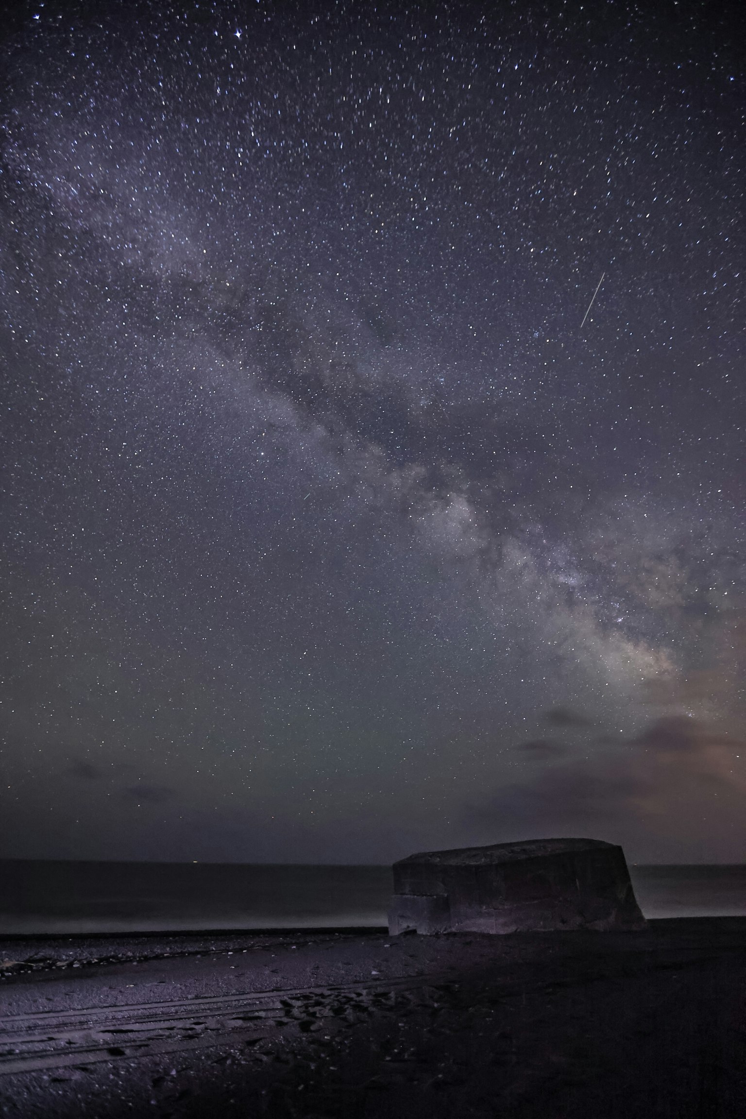 Vista mozzafiato della Via Lattea su una spiaggia con una silhouette scura in primo piano