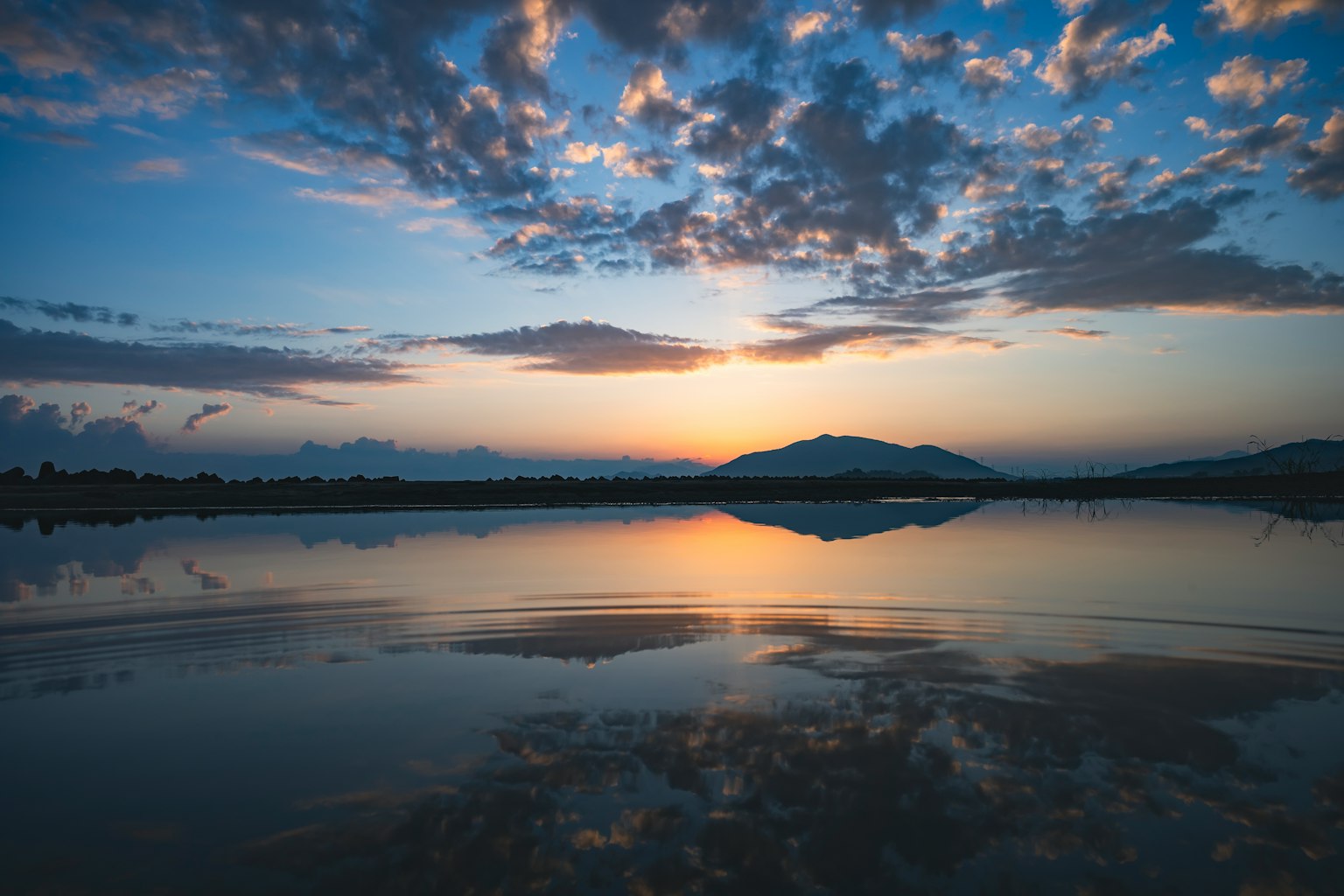Pemandangan indah matahari terbenam di danau dengan refleksi awan dan gunung
