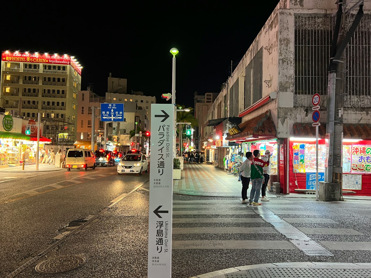 Street scene at night featuring directional sign and illuminated shops
