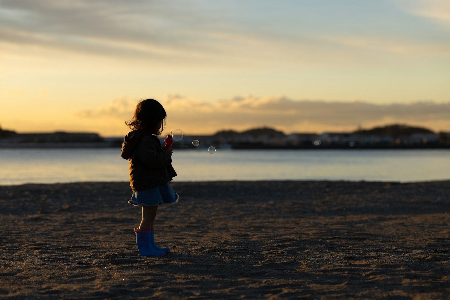 Anak berdiri di pantai dengan latar belakang matahari terbenam
