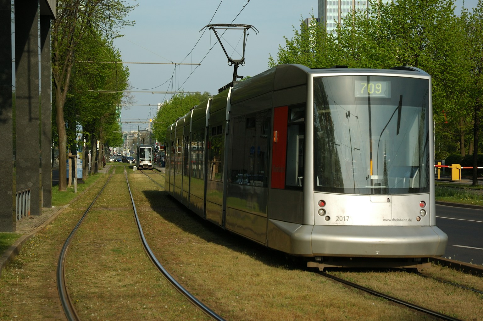 Un tram argenté arrêté sur des rails couverts d'herbe avec des arbres en arrière-plan