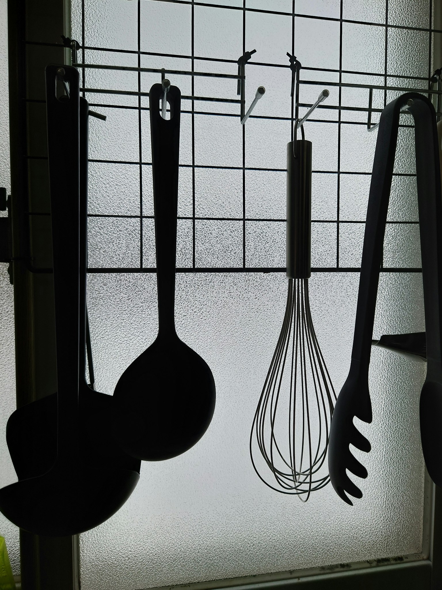 Silhouette di utensili da cucina neri appesi vicino a una finestra