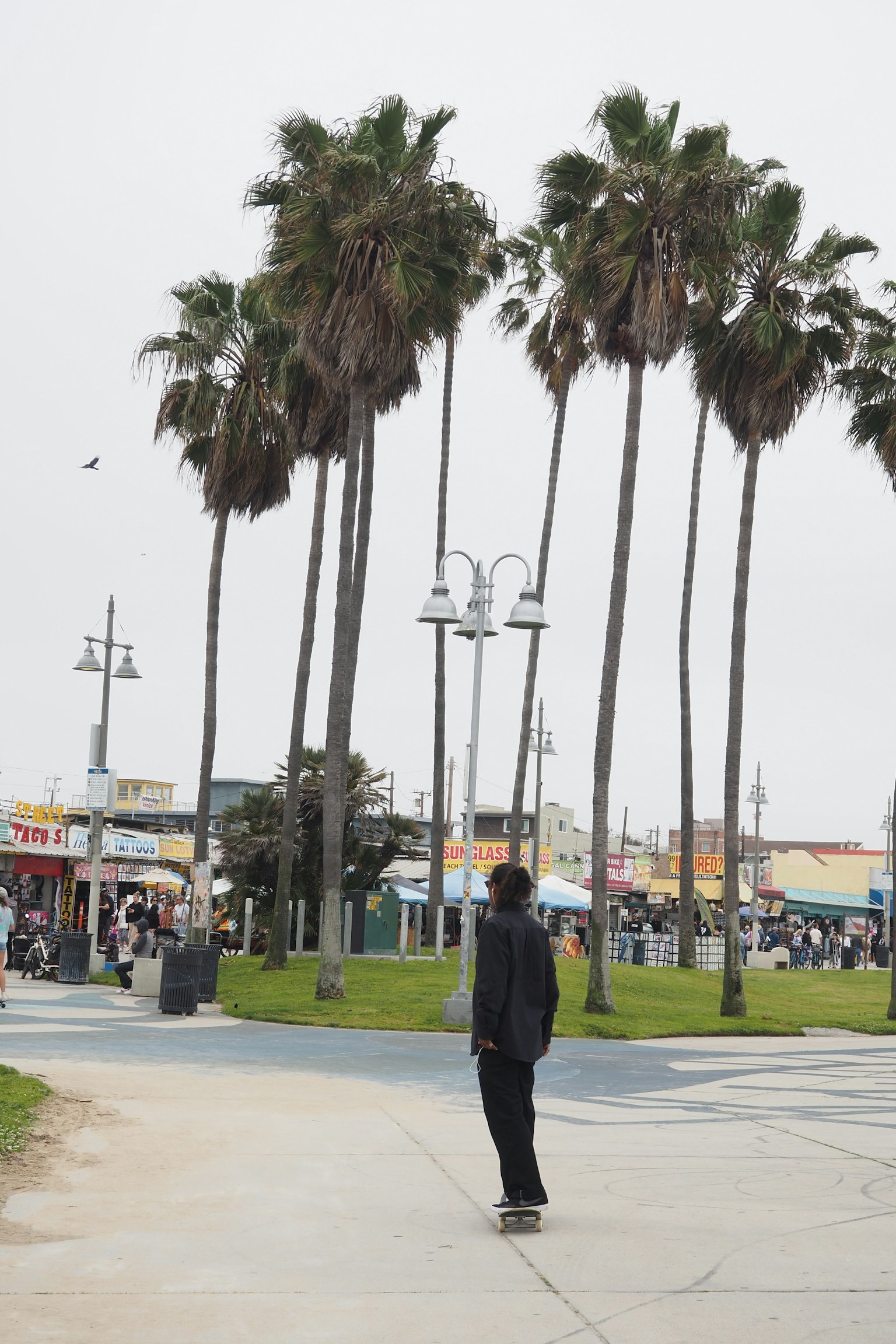 Une personne sur un skateboard dans une scène de plage avec des palmiers et des gens en arrière-plan