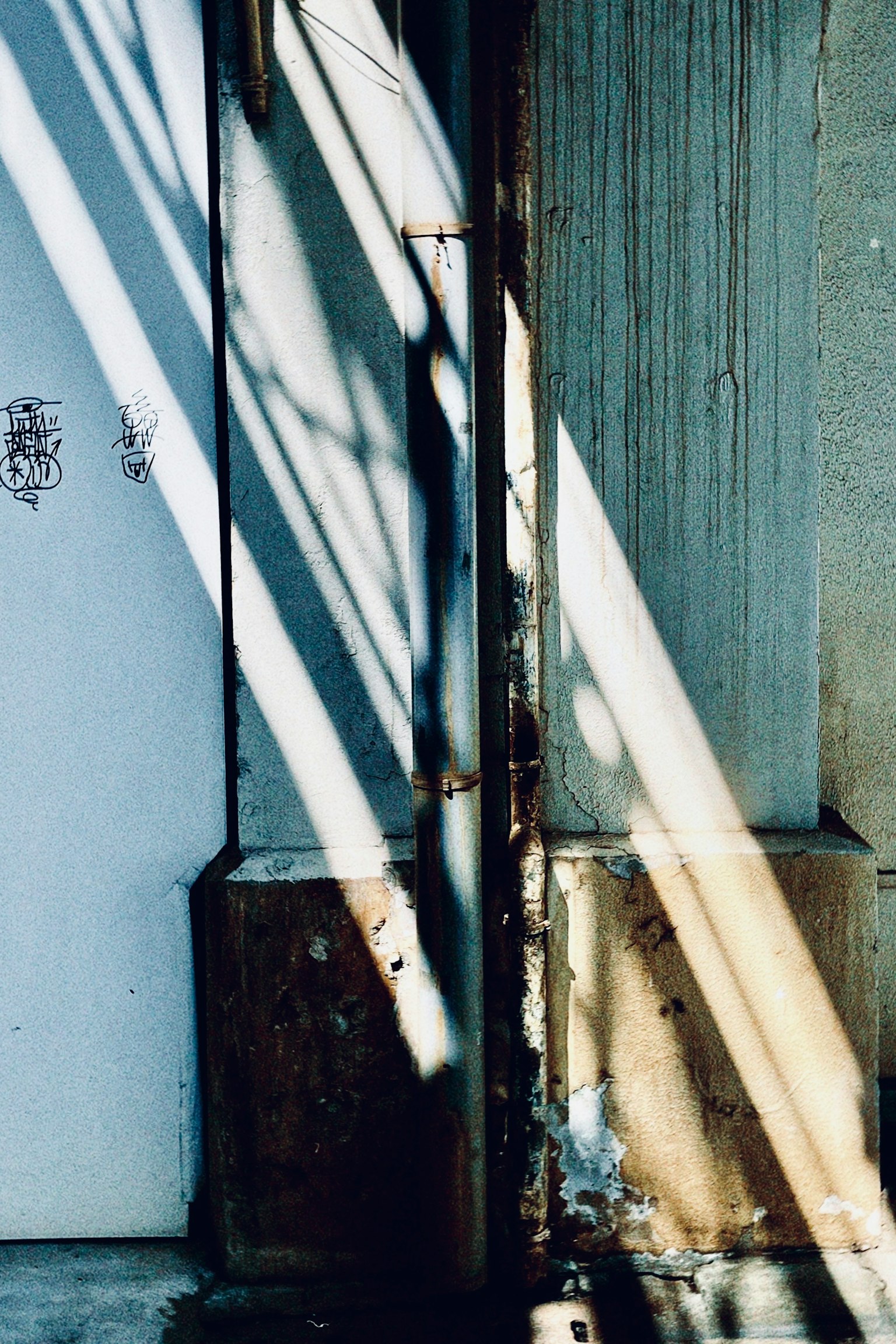 Detalle de una pared y una puerta con sombras y luz cruzadas