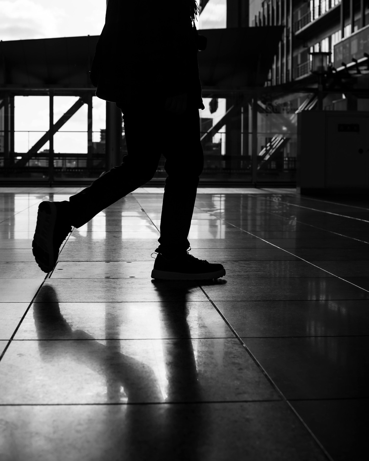 Silhouette di una persona che cammina riflessa su un pavimento lucido in bianco e nero