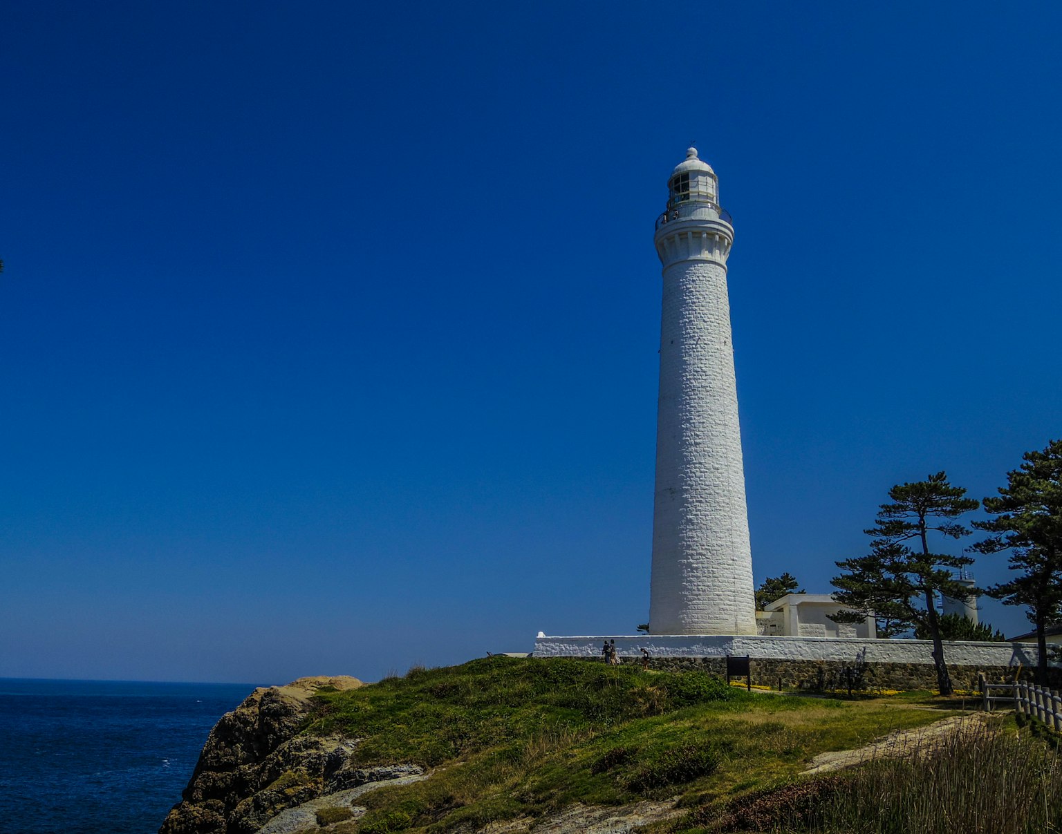 Weißer Leuchtturm am Meer unter blauem Himmel