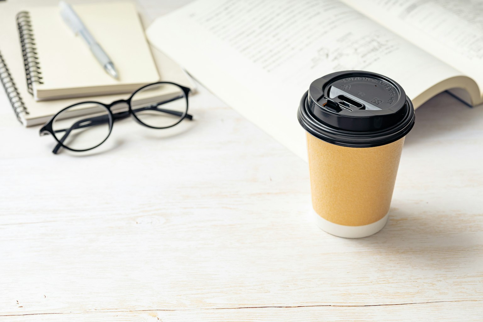 ถ้วยกาแฟบนโต๊ะพร้อมสมุดบันทึกและแว่นตา