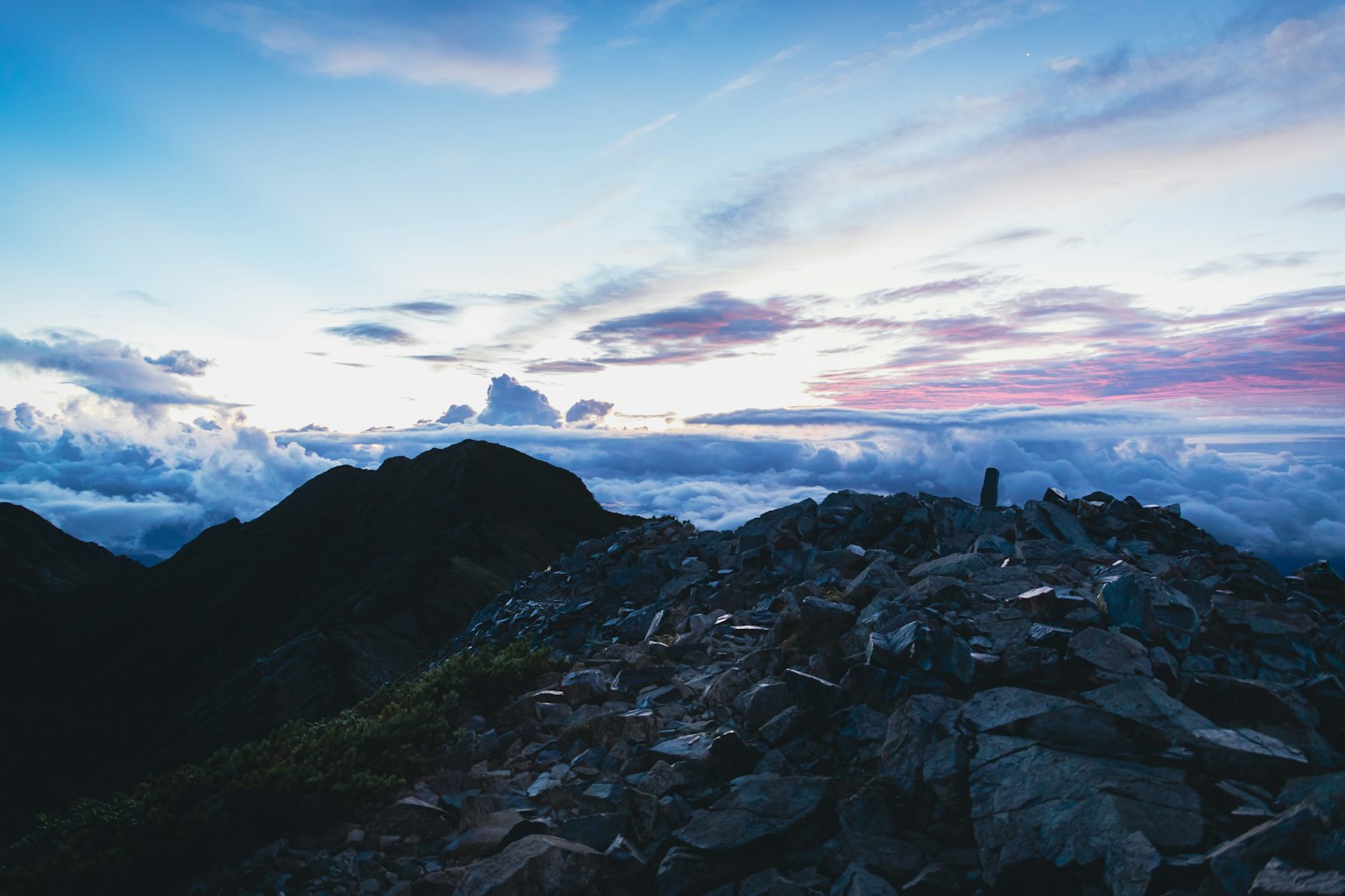 Vista mozzafiato del tramonto con una persona in piedi su una cima montuosa che guarda un mare di nuvole