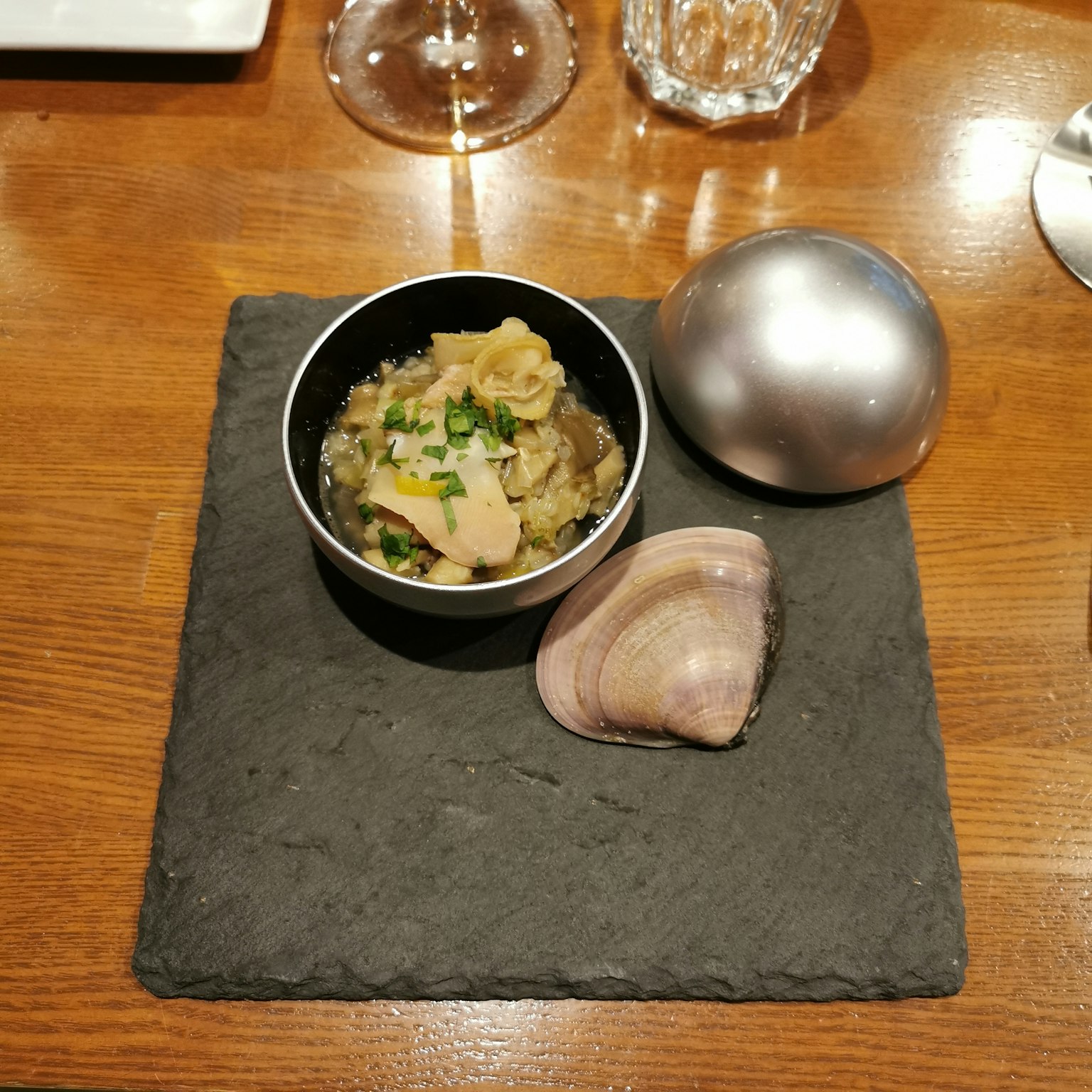 Piatto servito su un piatto nero con una piccola ciotola di frutti di mare e una sfera argentata