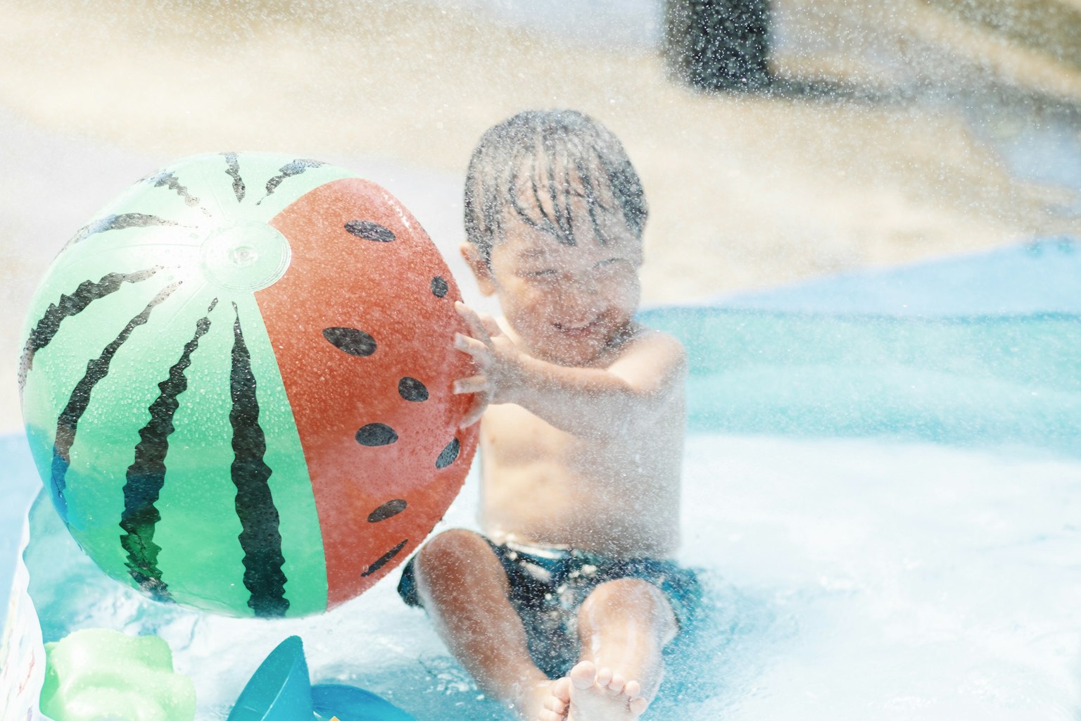 Child playing in water with a watermelon-patterned ball