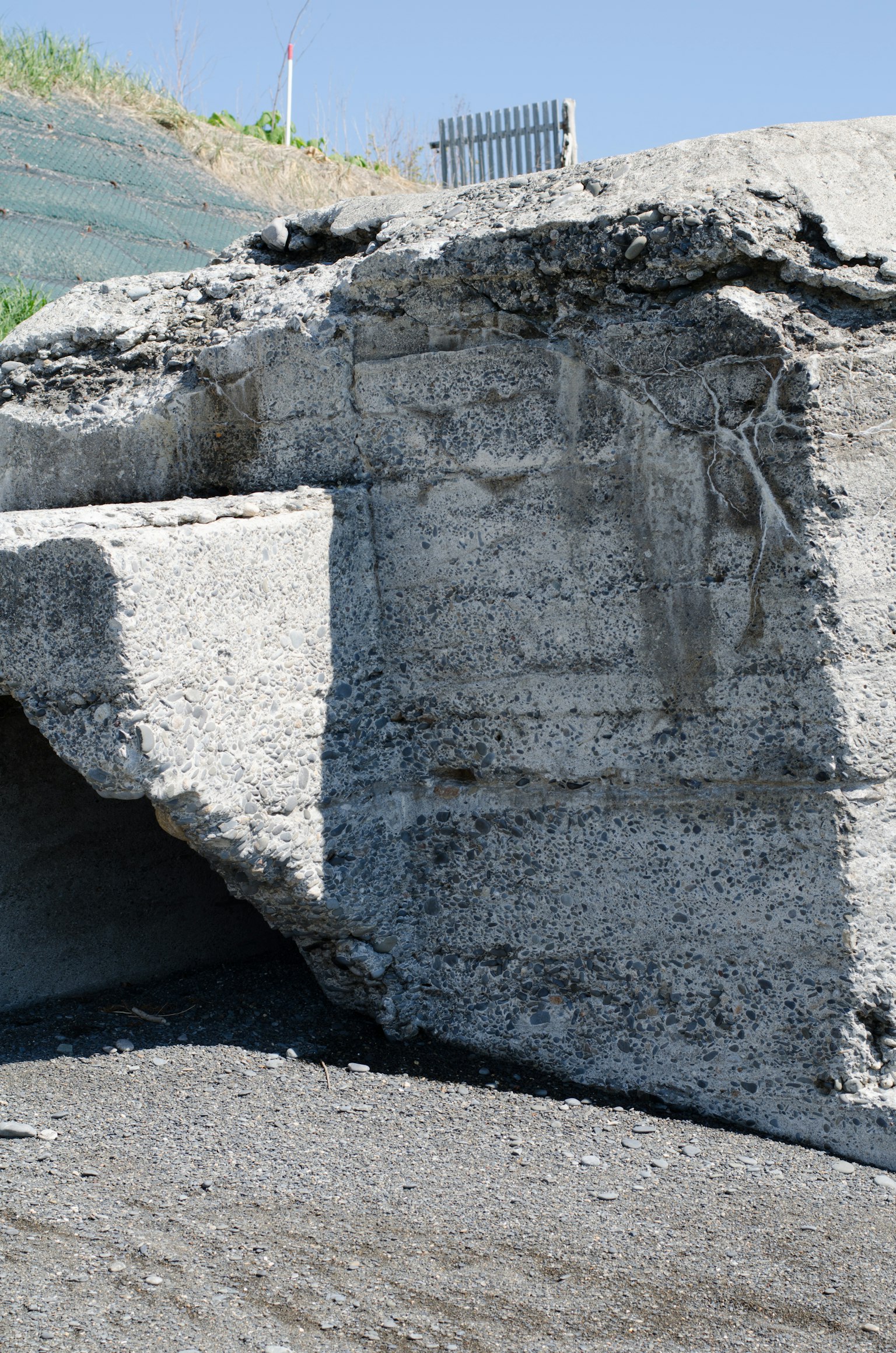 Image d'un grand bloc de béton avec des fissures à sa surface entouré de gravier