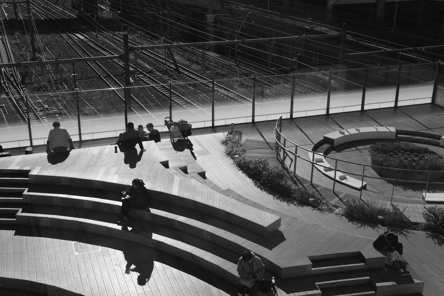 Schwarzweißfoto von Personen auf Bänken mit Bahngleisen im Hintergrund