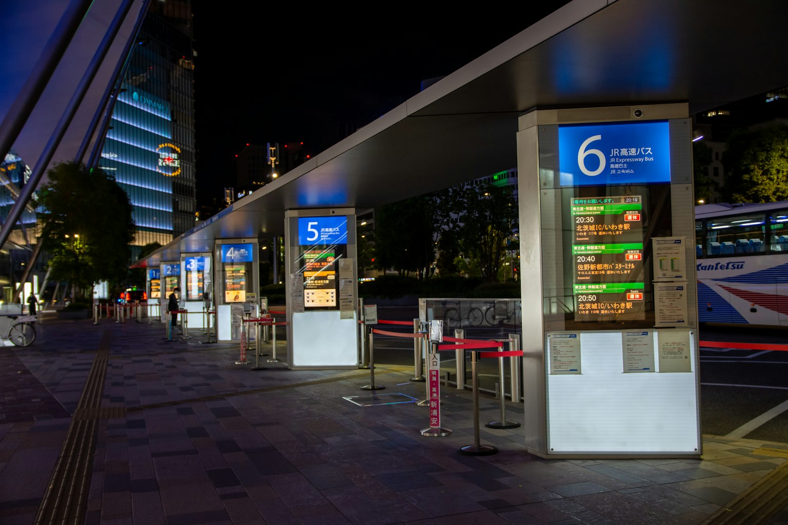 Night view of a bus stop with illuminated schedules and numbers nearby buildings visible