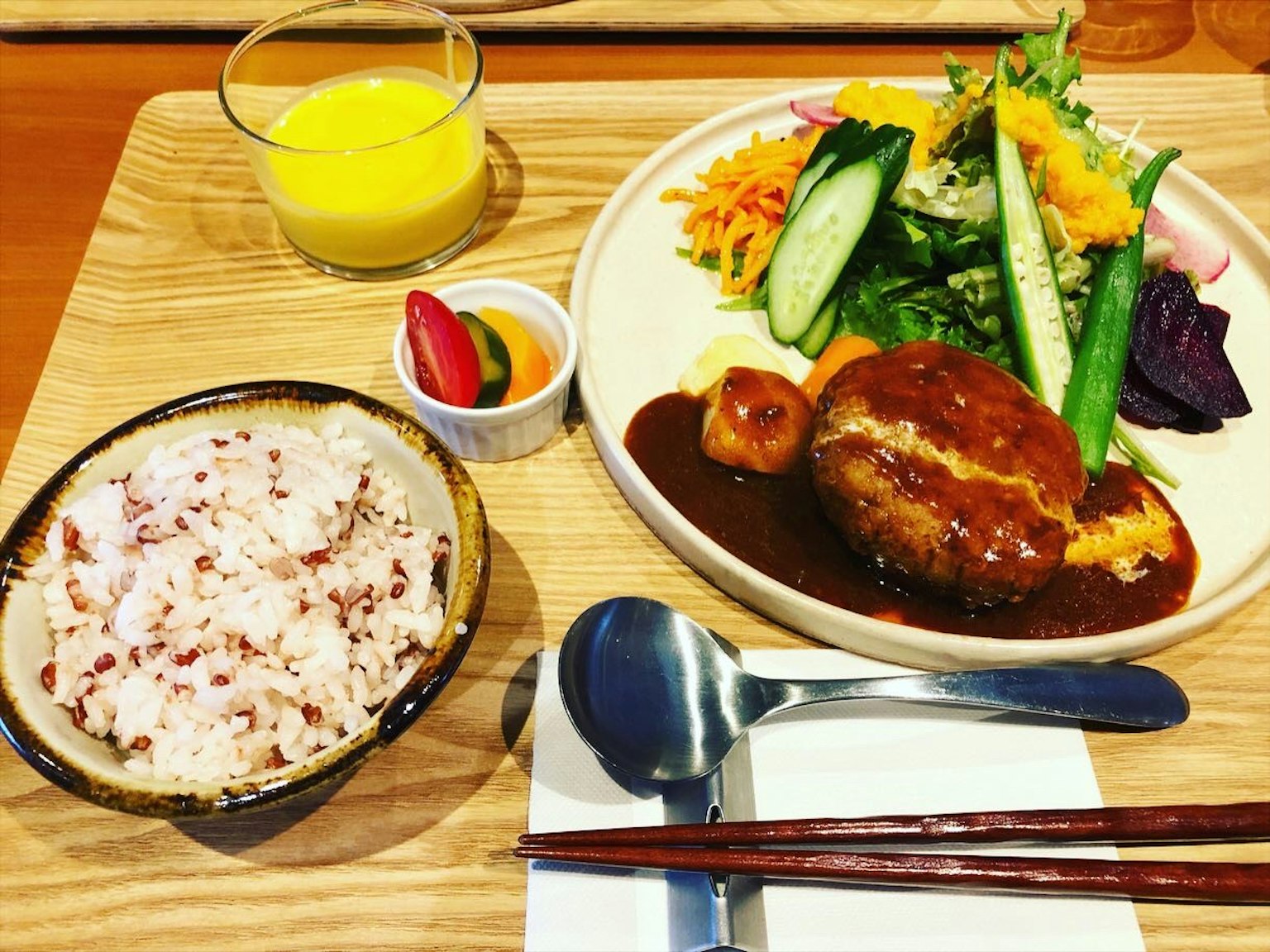 Delicious hamburger steak with salad, red rice, and orange juice arranged on a wooden table