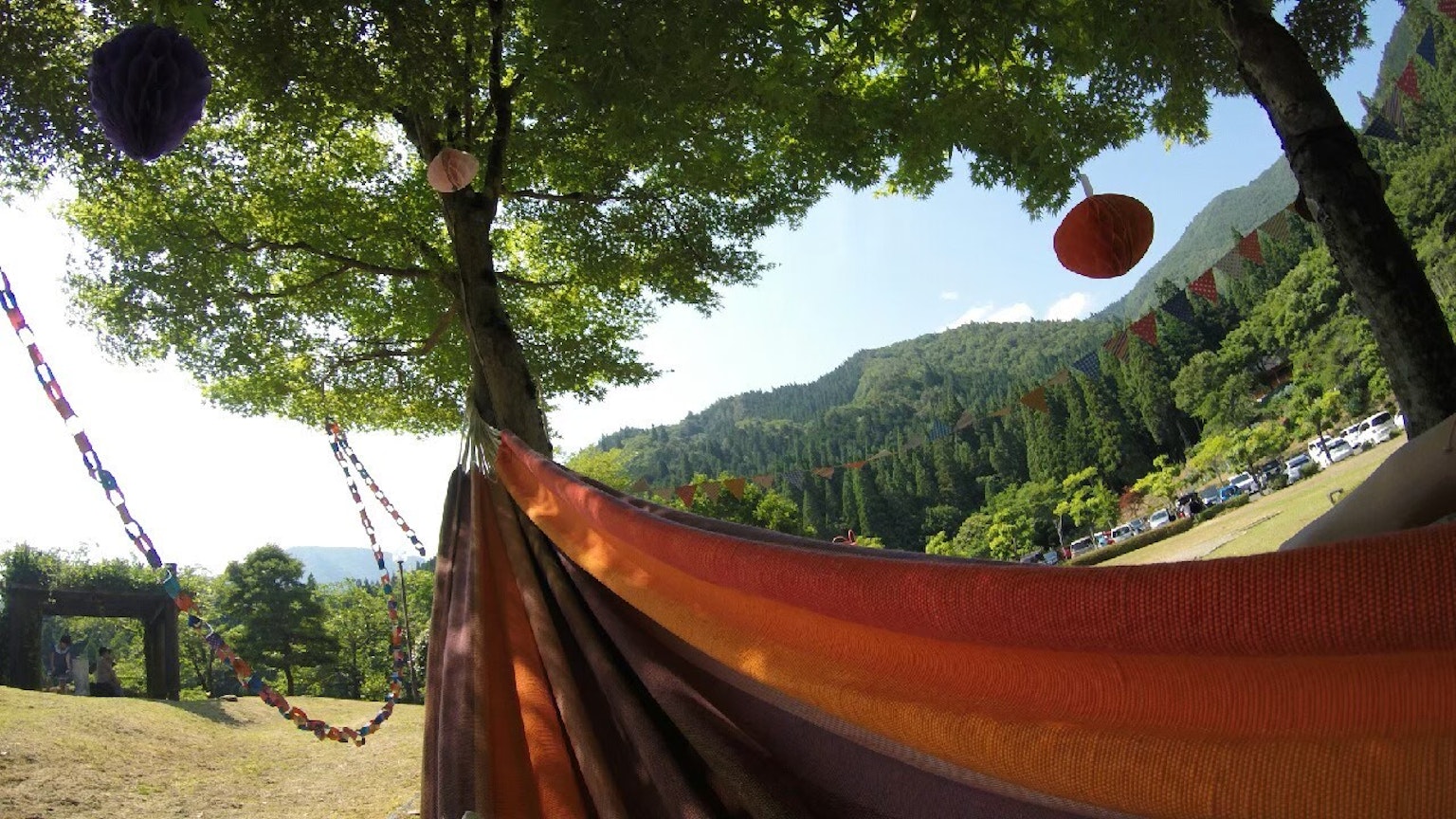 Amaca arancione appesa sotto un albero verde con sfondo montano