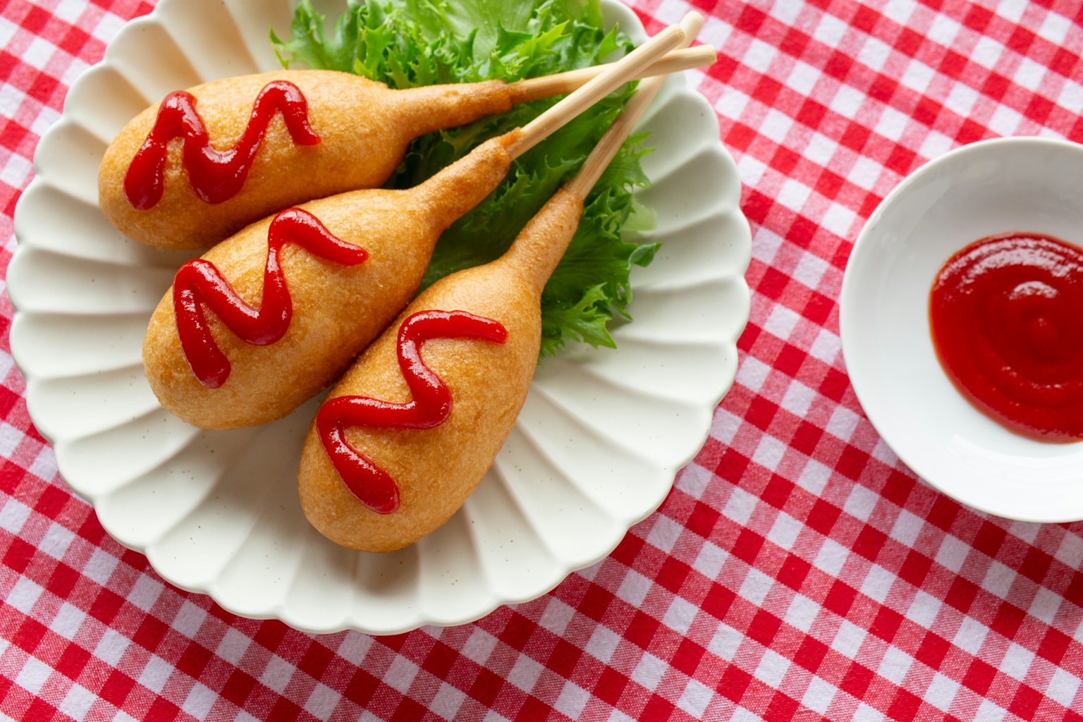 Tres corn dogs colocados sobre lechuga con decoración de ketchup