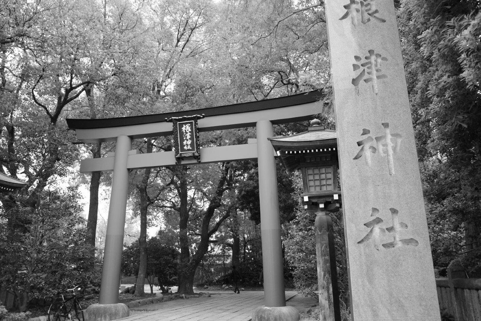 Pintu masuk kuil dengan gerbang torii hitam dan putih serta monumen batu