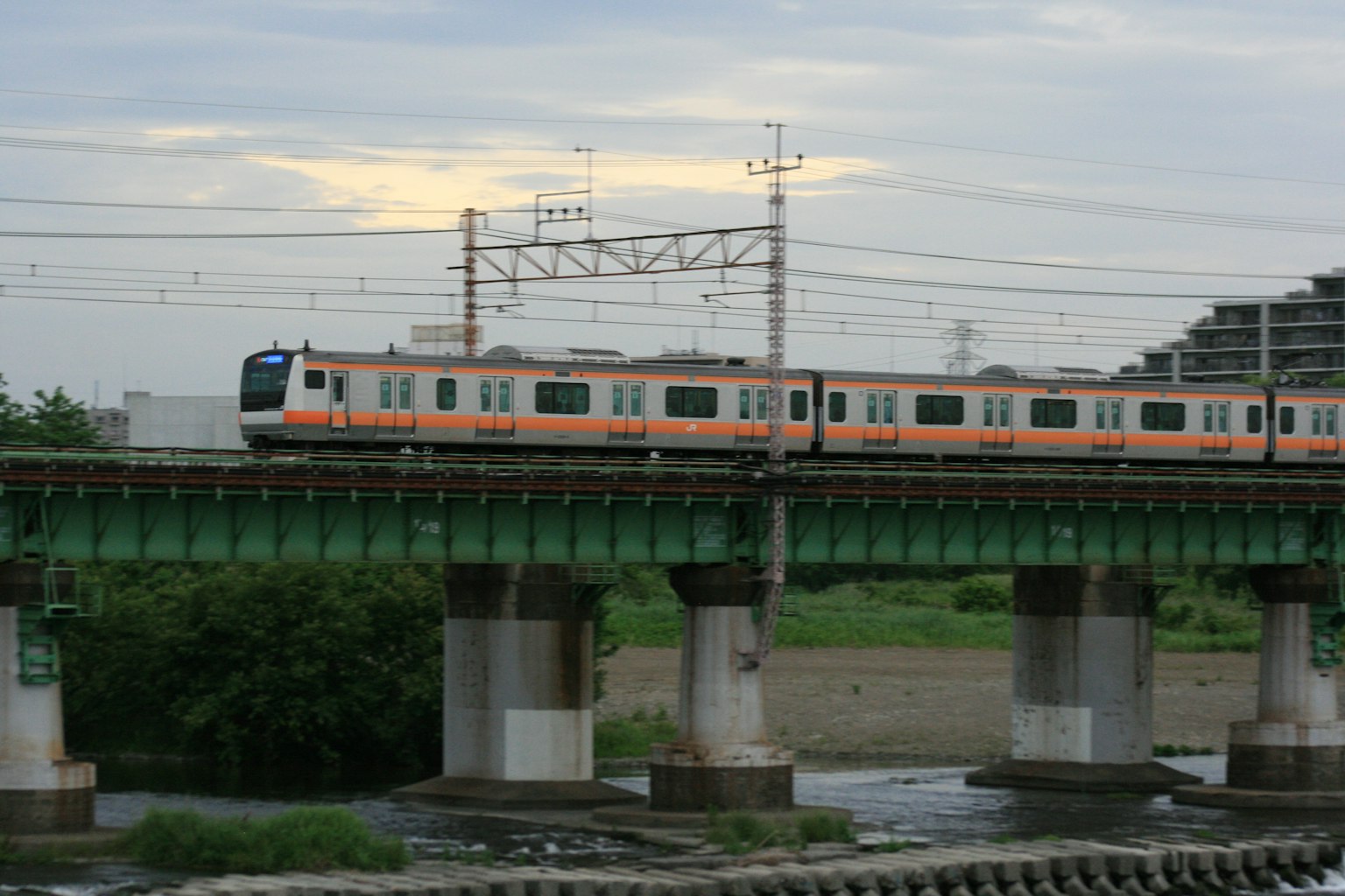 Train orange traversant un pont ferroviaire vert au-dessus d'une rivière
