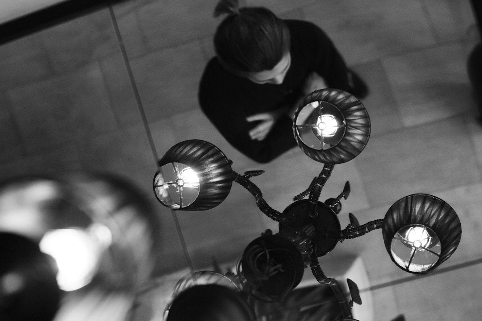 Black and white image from above featuring a woman and chandelier lights