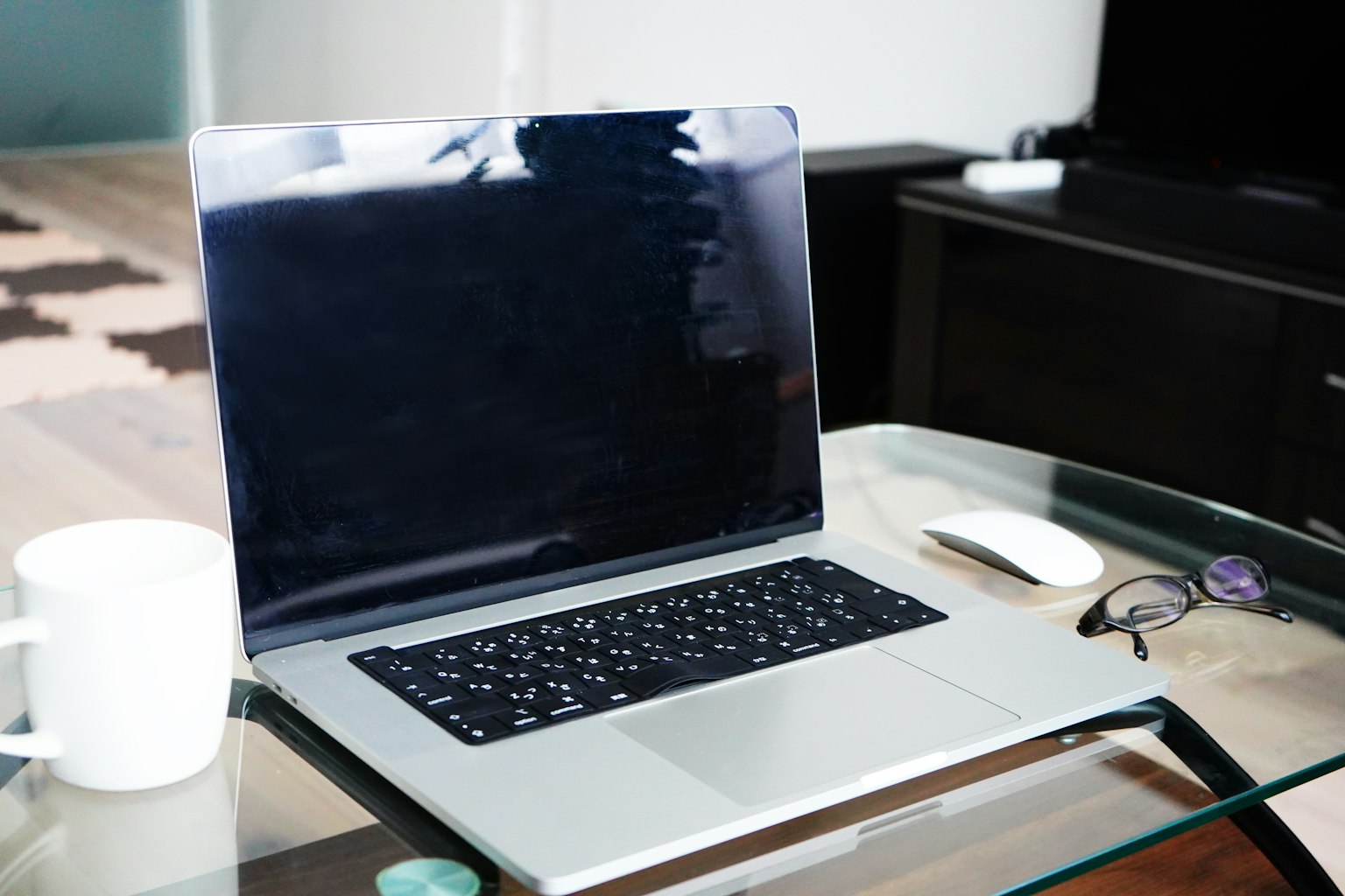 Laptop mit schwarzem Bildschirm neben einer Maus Kaffeetasse und Brille