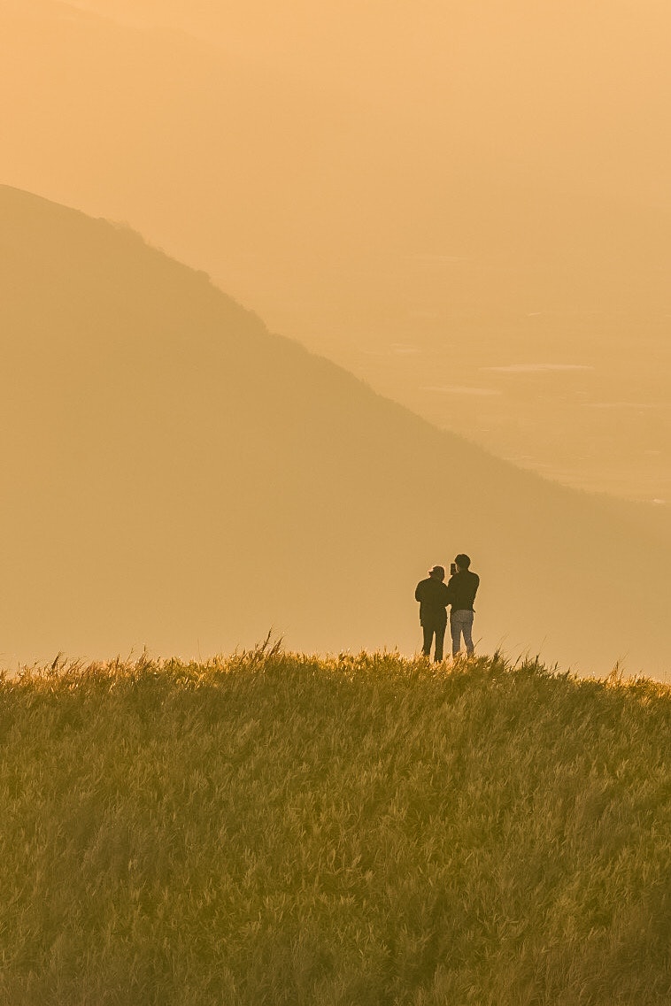 zwei Personen als Silhouette auf einem grasigen Hügel bei Sonnenuntergang