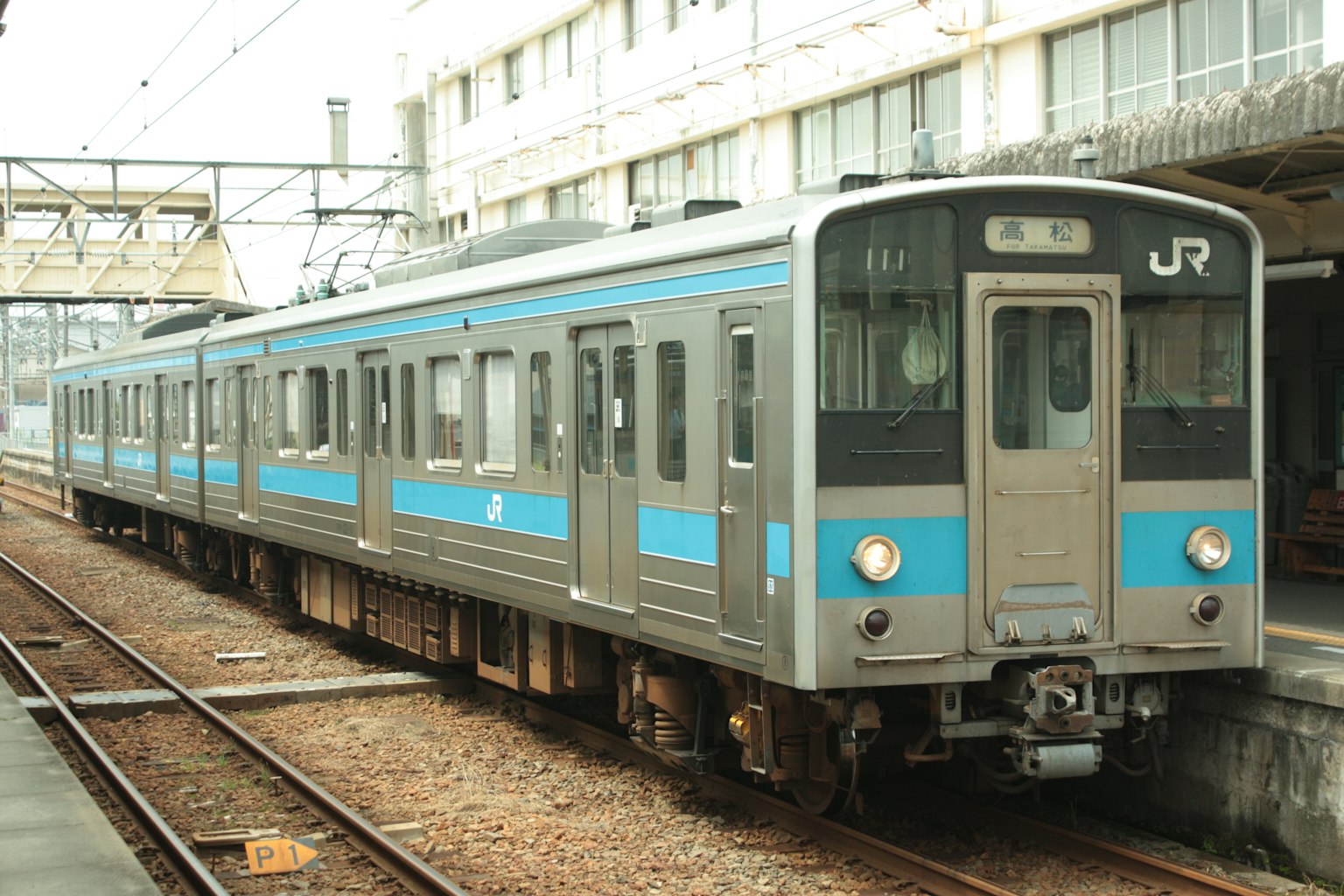 Silver JR train with blue lines parked at a station