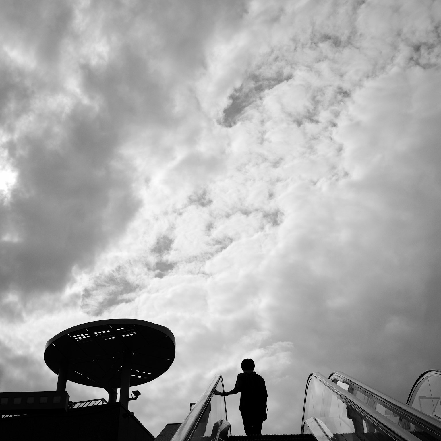 Silhouette di una persona che sale una scala mobile sotto un cielo nuvoloso