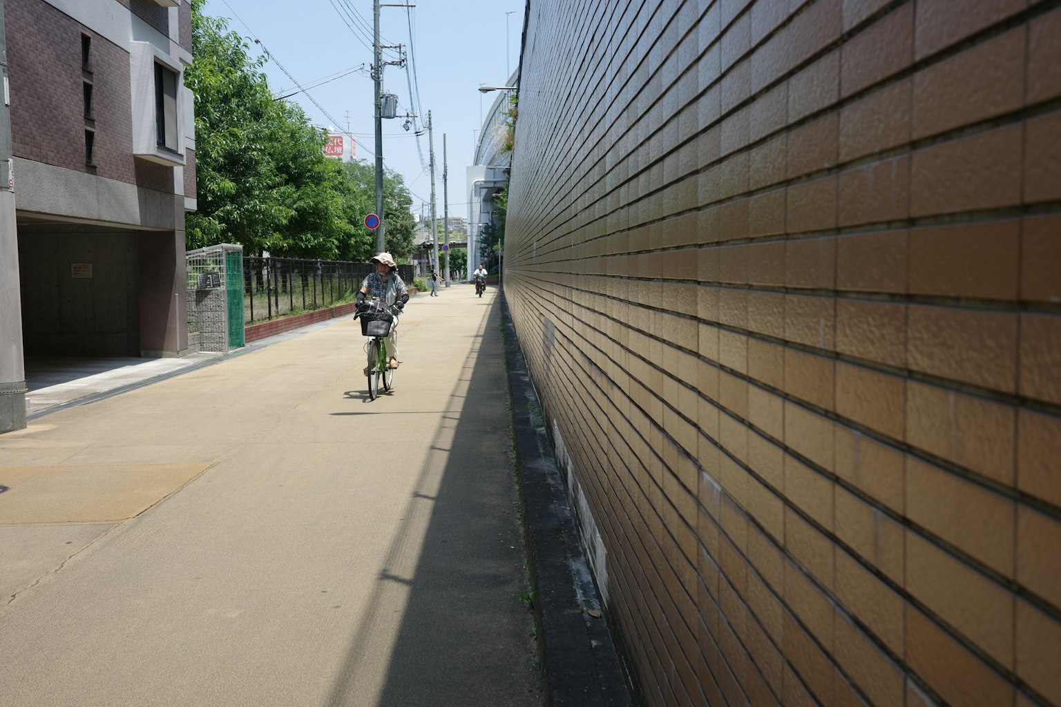 ทัศนียภาพในเมืองที่มีคนขี่จักรยานมีผนังอิฐทางซ้ายและต้นไม้ตามถนนทางขวา