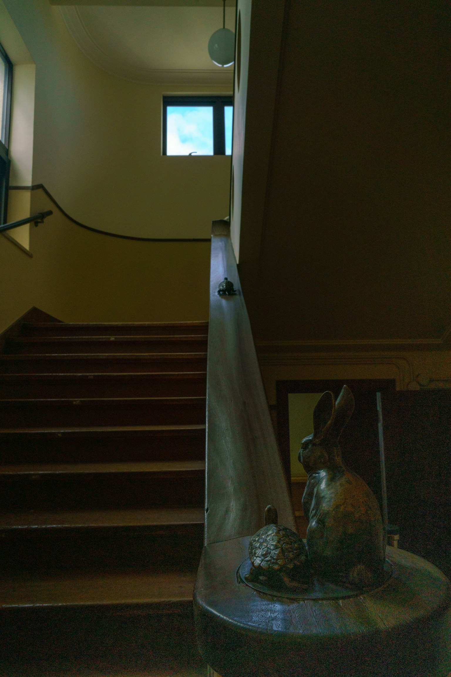 Vue intérieure d'un escalier avec une fenêtre en haut et une sculpture de lapin près de la rampe