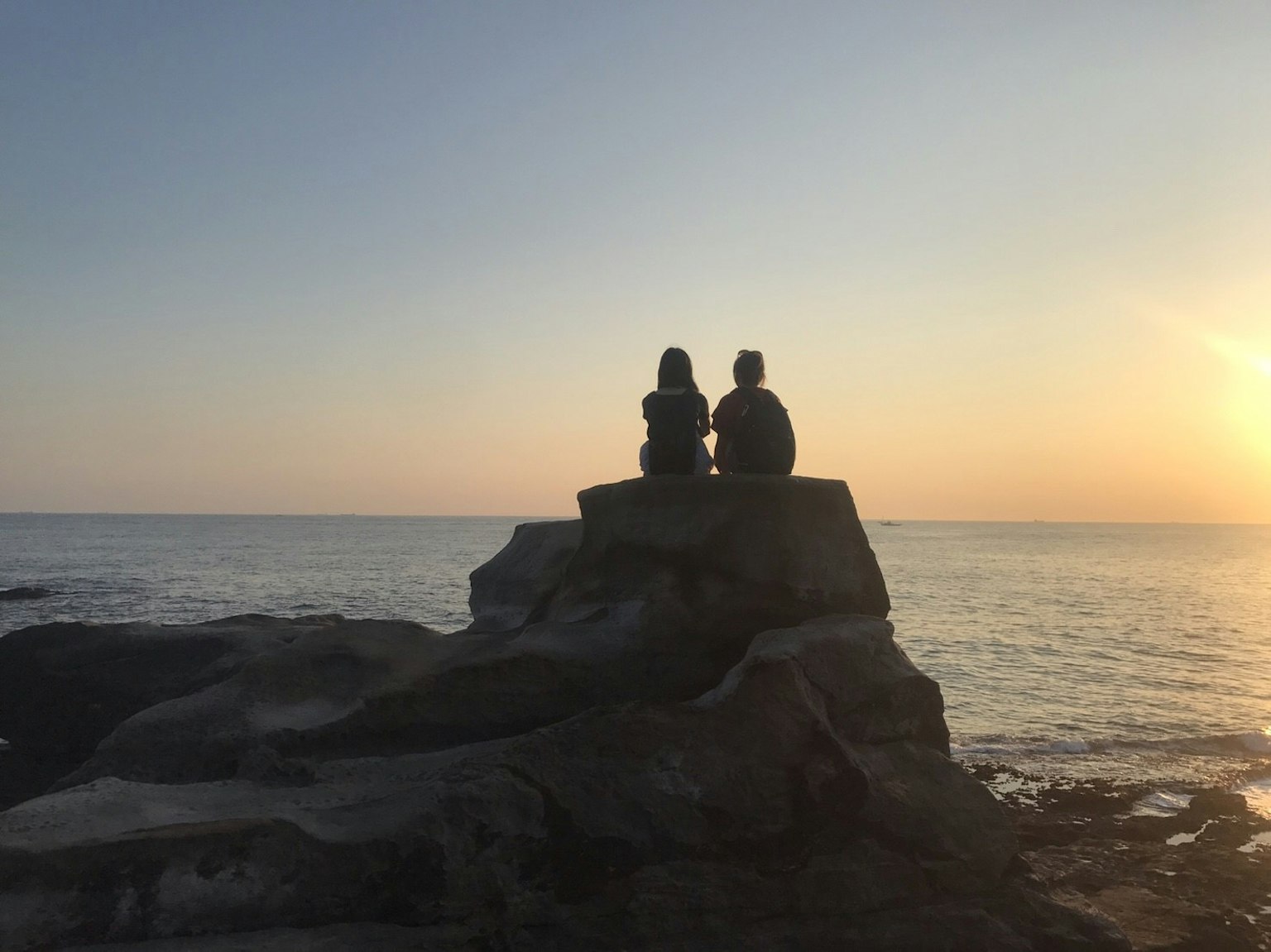 Silhouette di due persone sedute su una roccia contro un tramonto